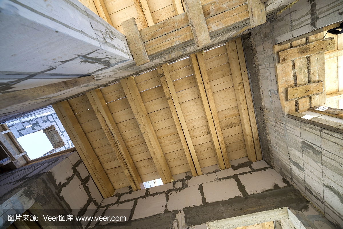 正在施工和装修的房间内部的特写细节。节能墙体采用中空泡沫保温砌块,木质天花板梁为屋顶框架。